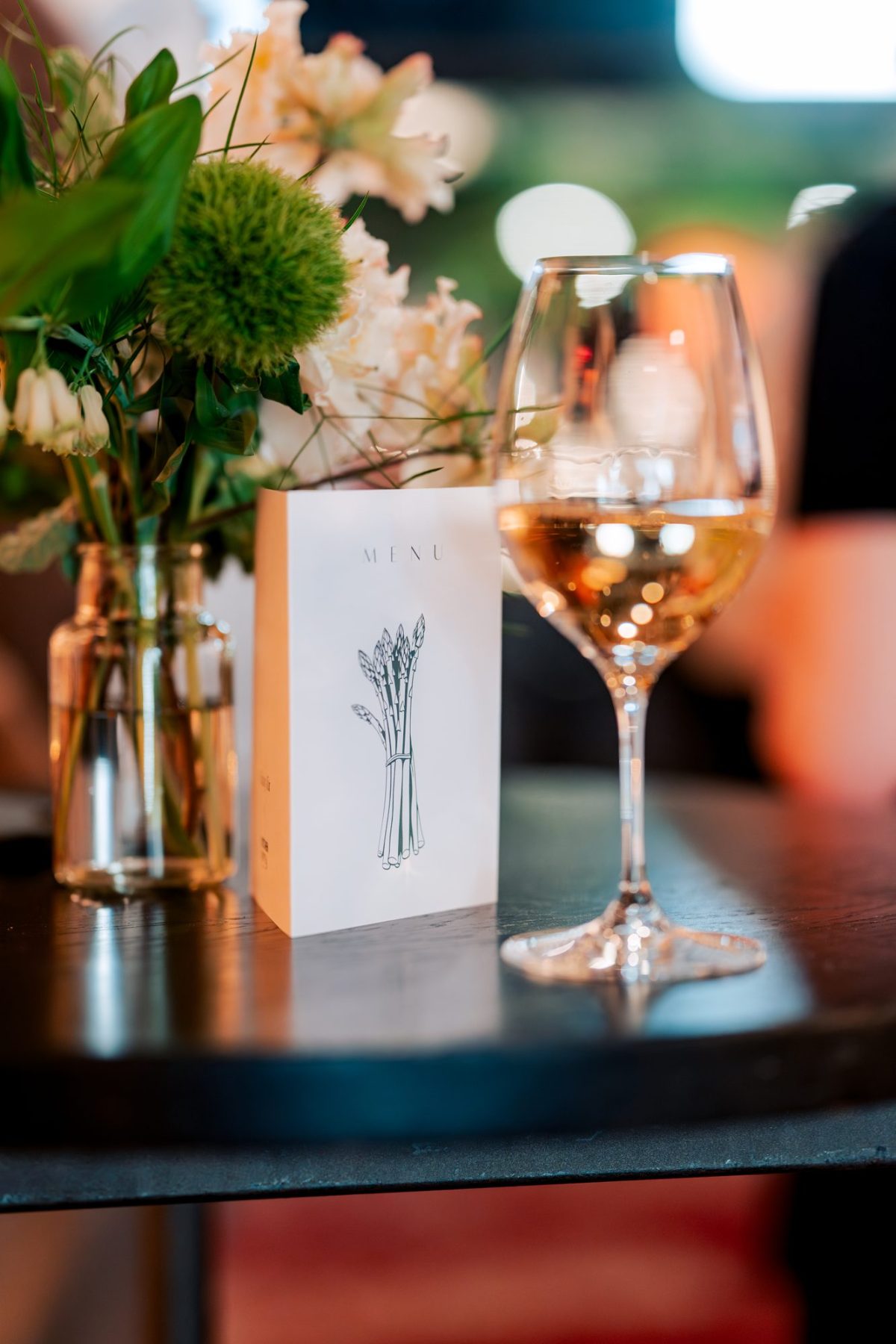 Asparagus menu card and a glass of white wine on a table at KITCHEN 55